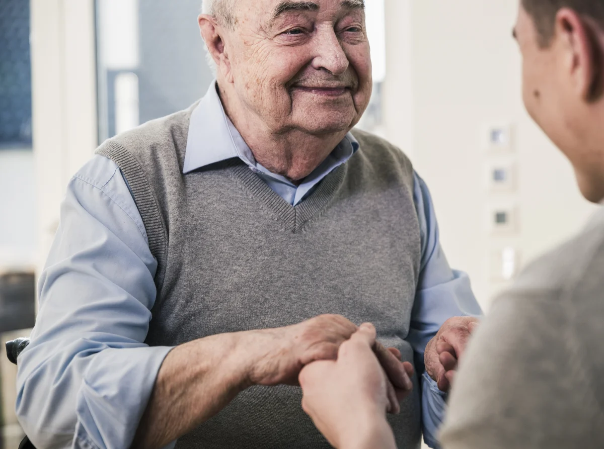 senior man smiling at young man holding his hands